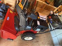 Full side view of red metal housing, black chute, engine and tires