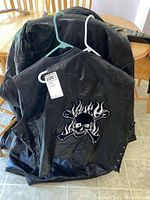 Black leather vest with skull and flame crossbones patch on back, and black leather jacket behind it on hanger.