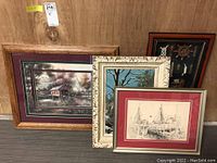 Four pieces of wall art including covered bridge print, painted winter scene, nautical shadowbox, and Gloucester boat yard drawing arranged together on a wood background.