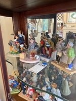 Multiple Norman Rockwell inspired porcelain figurines displayed on glass shelves, depicting various characters in different poses.