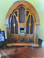 Front view of the vintage AM/FM radio showing the wooden cathedral style cabinet with decorative speaker grille and three control knobs.