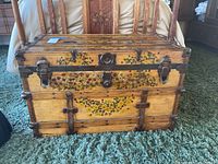 Front view of the antique wooden trunk showing painted floral patterns and metal latches