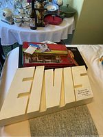 Photo showing large white plastic Elvis display piece on table with other Elvis related items and additional collectibles in background.