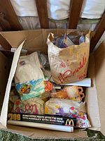 Top-down view of a box showing various McDonald's Happy Meal collectibles including paper bags, plush toys, and enclosed items.