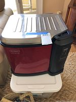 Red Butterball electric turkey fryer with stainless steel lid seen from front and side, placed on a plastic container.