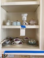 Photo of porcelain cups, saucers, lidded vessels, and decorative footed vase on shelves.