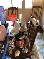 Wide view of the collection on a wooden table including decorative mugs, figurines, glassware and other home decor items.