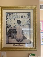 Full view of framed Diego Rivera print depicting a nude woman kneeling with white flowers in baskets, signature visible.