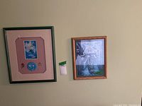 Two framed artworks affixed to wall, one with Disney The Little Mermaid theme and enamel pins, the other with Barbie print
