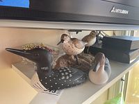 Four wooden bird figures displayed together on a shelf with electronic devices nearby