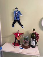 Photo showing three Elvis Presley figures and a bottle with Elvis image on the label.