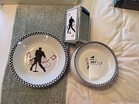 Photo showing two white bowls with black and white checkered rim and Elvis Presley silhouette design with musical notes, placed on a table.