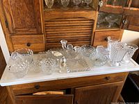 Full view of all Forstoria Early American pattern glassware displayed on white surface showing bowls, candlesticks, cream pitcher, salt shaker, and serving dishes.