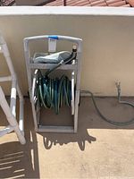Wide view showing the garden hose coiled on gray plastic hose reel with handle, attached spray nozzle on top.