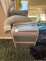 Haier portable air conditioner unit with flexible white exhaust hose and remote on top, silver color with minor surface wear.