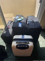 Four large suitcases of different sizes arranged on a green carpet near a window, one beige and three black.
