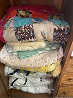 Stack of comforters and quilts showing various colors and patterns including patchwork blue tie-style and pastel florals.