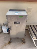 Front view of Masterbuilt electric smoker showing temperature gauge, spring handle on door, base legs with rust.