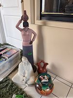 Full view of the three sculptures and two pottery vessels arranged on floor near fireplace.