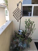 Wide shot of large potted succulent plant with metal bell holder and bells hanging in diamond grid shape