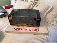 Premiere Edition Maisto Hummer SUV model box on top of Newportopoly board game box on a bed with pillows.