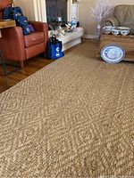 View of the full 10x14 natural fiber jute area rug laid out on a hardwood floor in a living room setting near furniture.