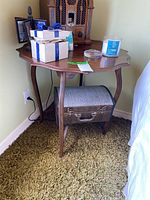 Front view of wooden side table showing scalloped top edge and curved legs with fabric storage chest underneath