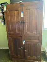 Front view of vintage wooden icebox showing four paneled doors with metal latches and hinges, plus visible wear.