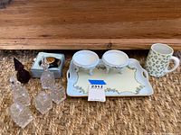 Photo of glass salt and pepper shakers, glass vinegar and olive oil bottles, glass toothpick holder, porcelain tray with two small bowls, and a porcelain mug with clover pattern.
