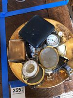 Overview of round decorative metal tray holding assorted travel clocks, pocket watches and wristwatches