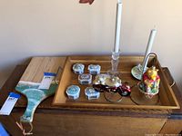 Photo of wooden serving tray holding decorative ceramic boxes, glass candlesticks, a figurine, and a small motorcycle model.