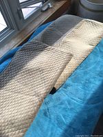 Two gray quilted pillow covers laid out on a blue surface, showing the diamond quilting texture and their size for European pillows.