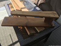 Photo showing a decorative antique wooden ironing board with two flat planks and handle, placed on a wicker outdoor table.