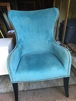 Front view of a blue wingback chair upholstered in textured blue fabric with metal nailhead trim, black legs, shows slight wear.