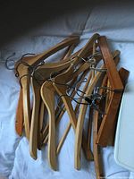 Pile of several wooden coat hangers, some with metal clips, placed on a light colored fabric surface.