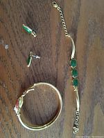 Photo of gold-tone earrings with green teardrop stones, gold-tone bracelet with three green square stones on chain, and gold-tone fish design bangle bracelet.