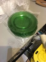Stack of green glass plates showing color and texture, wrapped partially in bubble wrap on table.
