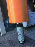 Side angle of the lamp showing the orange lampshade and hand-painted ceramic base with dot patterns