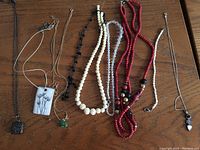 View of seven assorted necklaces laid out on wooden surface showing different designs and bead styles