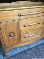 Front angled view showing two doors with round knobs, three drawers with elongated wooden handles, showing wood grain and curved bottom apron.
