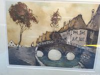 Lithograph artwork showing a small village with a multi-arched stone bridge over a waterway, houses and trees, in muted brown and beige colors.