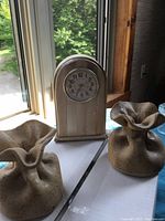 Photo showing mantel clock and two decorative pottery pieces with ruffled tops on a table near window light.