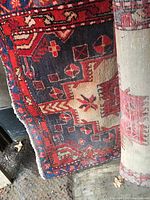 Close-up of the rug runner showing the geometric red, black, and cream design and texture, with the rug partially rolled.
