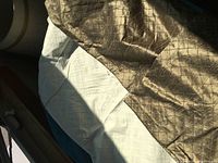 Drape laid out showing the gold silk outer fabric with a square embossed pattern and the white lining inside.