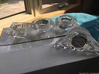 Three different shaped clear crystal tea light candle holders and one clear crystal clock on a white box near window light
