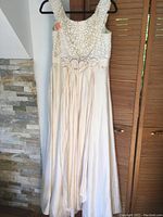 Front full view of the wedding dress hanging on a hanger, showing the lace bodice and flowing raw silk skirt.