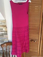 Full view of sleeveless pink dress hanging on wooden hanger with solid bodice and patterned skirt.
