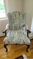 Front view of vintage upholstered armchair with floral fabric and carved wooden legs and arms.