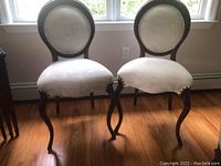 Pair of wood-framed round back upholstered accent chairs side by side on hardwood floor near window