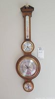 Full view of the wooden wall-mounted barometer including thermometer, clock, and smaller dial below. Shows overall design and size.
